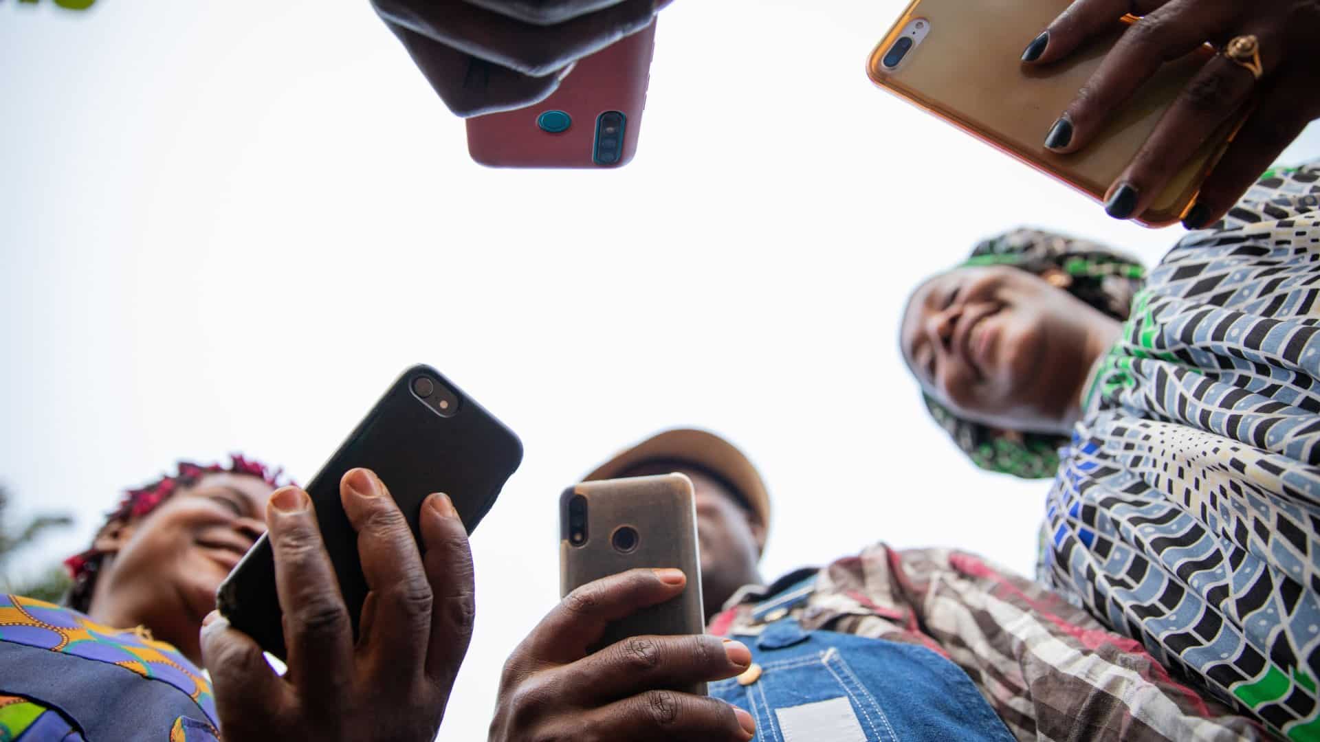 People seen from below laughing and looking at their phones against a bright sky